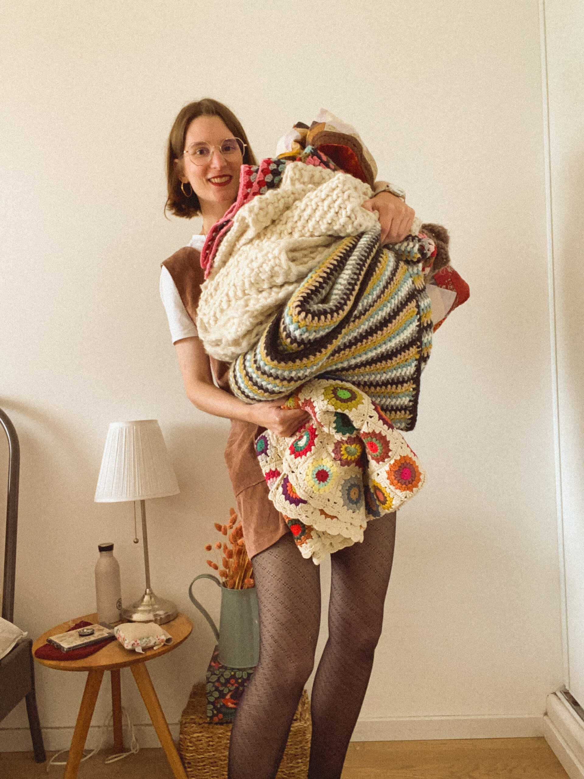 Une femme portant des couverture en patchork, crochet et tricot dans ses bras